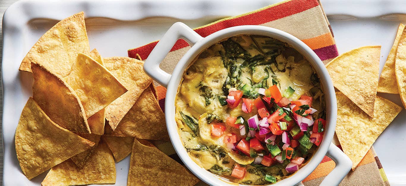 Cheesy Vegan Baked Spinach Dip on a white platter which a striped kitchen towel and backed tortilla chips