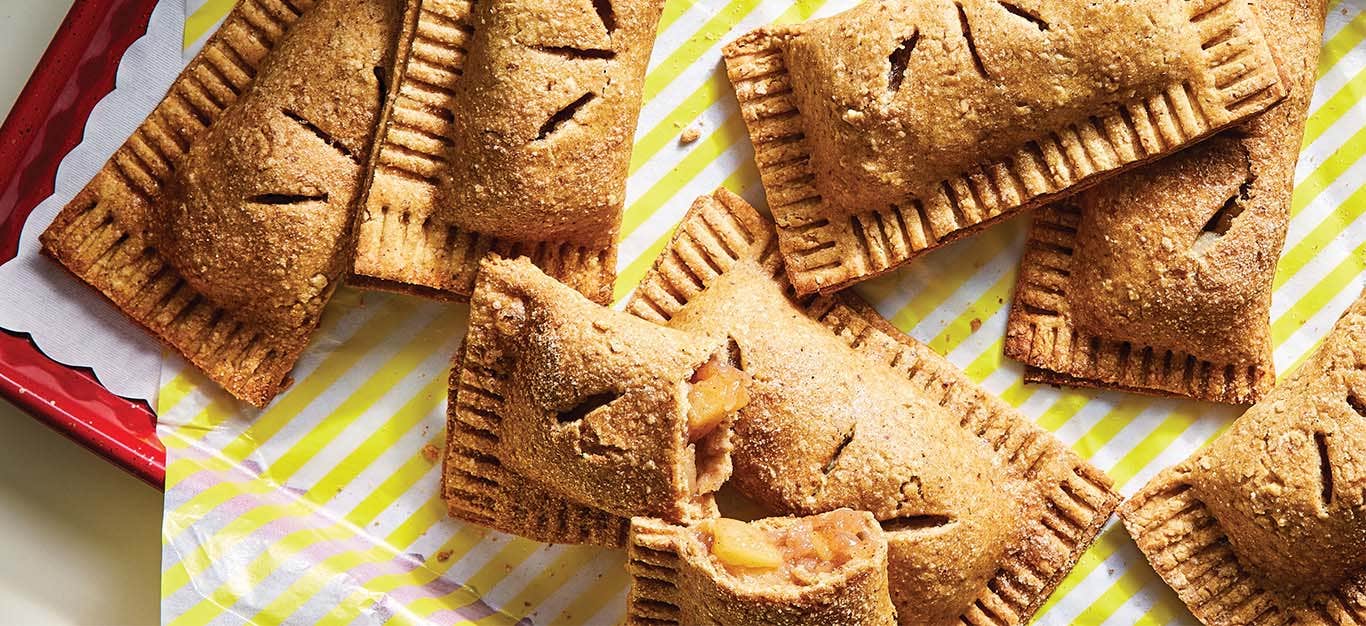 Vegan Cinnamon Apple Hand Pies on white and yellow striped paper on a red tray. One of the pies is broken showing the apple filling.