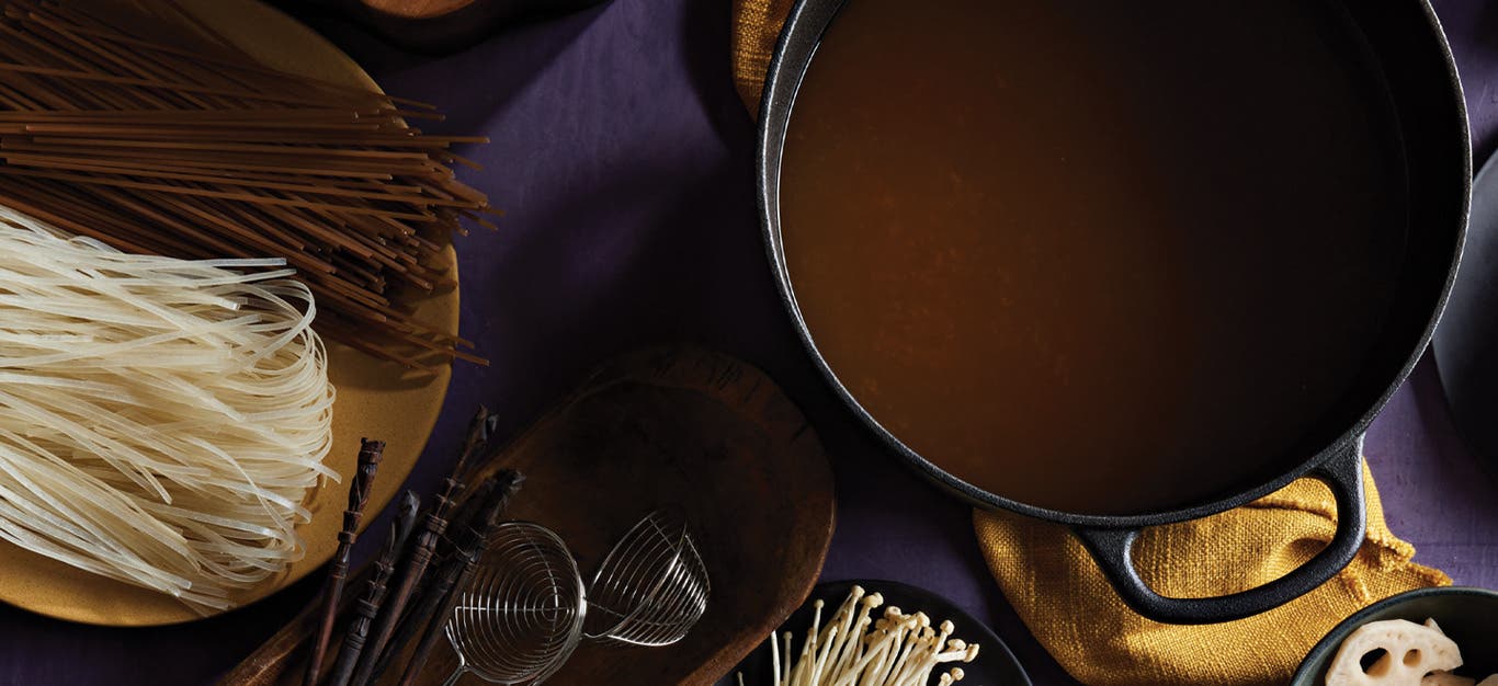 Sweet and Sour Vegan Hot Pot Broth in a cast iron pot next to dried soba and brown rice noodles