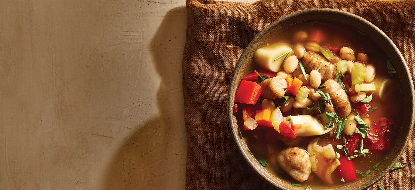 A bowl of Trumpet Mushroom, White Bean and Gnocchi Stew on a brown cloth napkin, ready to eat