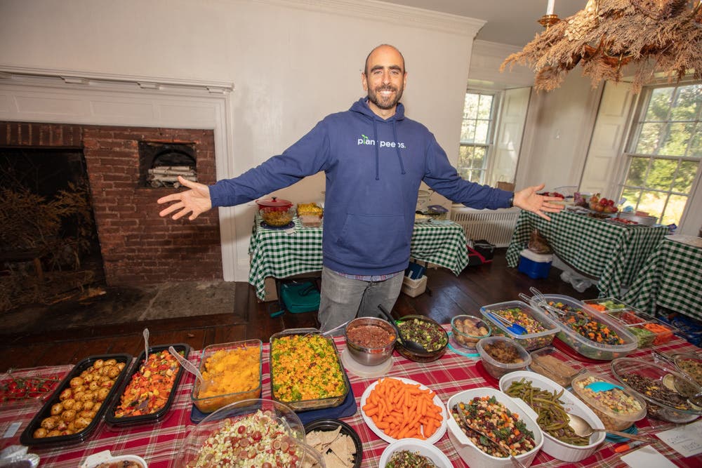 Love.Life Telehealth Founder Anthony Masiello stands behind a table with a bountiful spread of whole food plant based dishes, with his arms outstretched