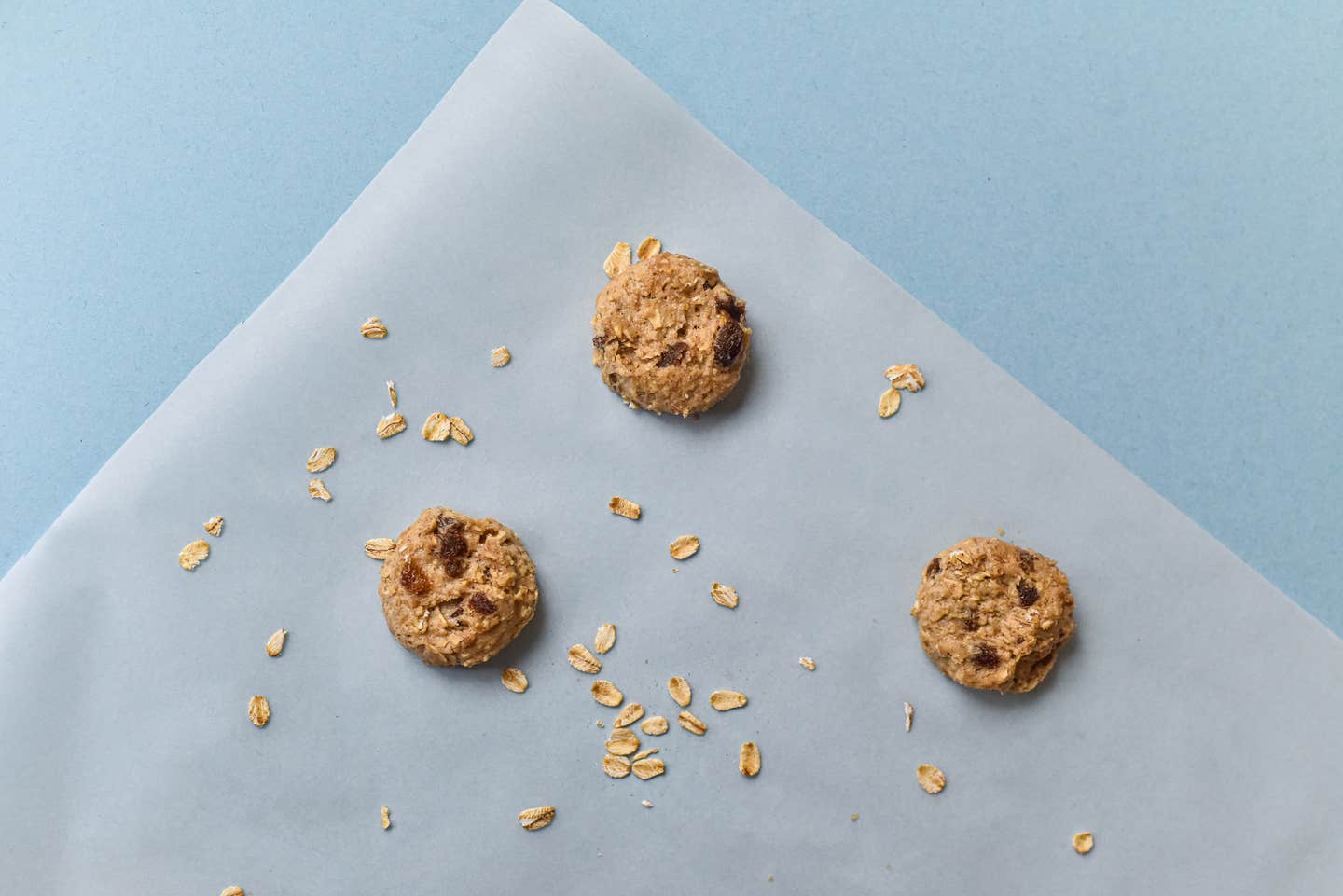 Three oat cookies on a parchment paper square with a blue background