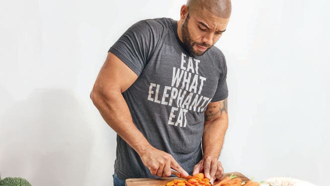 Dom Thompson chops carrots and wears a shirt that says Eat What Elephants Eat