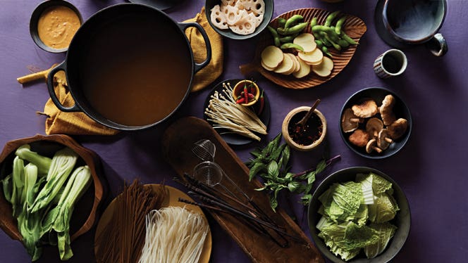 A spread of ingredients and tools for Vietnamese hot pot, including a large pot of broth and an assortment of add-ins such as fresh mushrooms and greens and lotus root