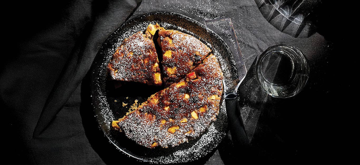 Top-down view of Air-Fryer Apple Fritter Cake dusted with powdered sugar, on a grey tablecloth next to a class of water