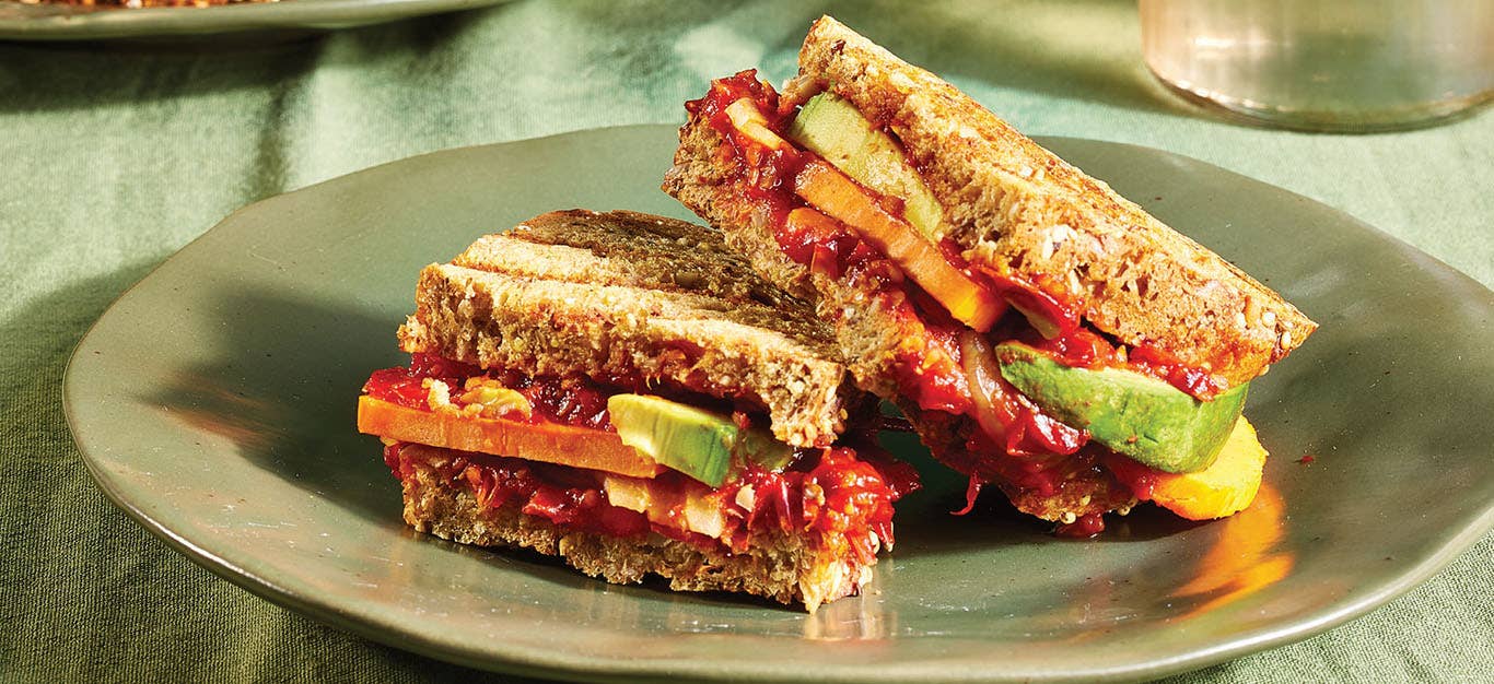 Avocado and Cherry Tomato Jam Panini cut in half with one half on top of the other, served on an earthy green ceramic plate