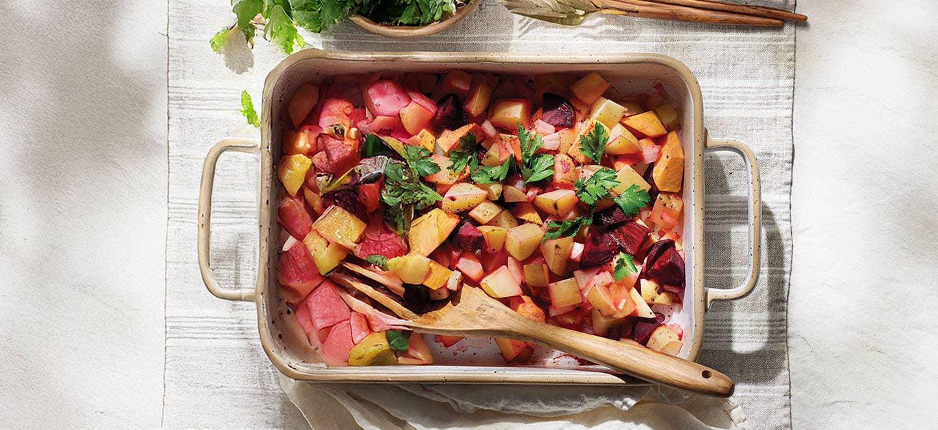 An oven tray of Vegan Red Flannel Hash on a pale grey kitchen town with a wooden serving spoon resting in the dish