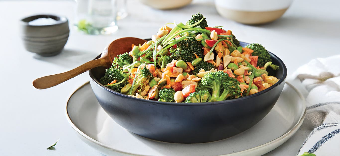 Broccoli Crunch Salad in a black bowl against a white background, with a wooden spoon in the bowl