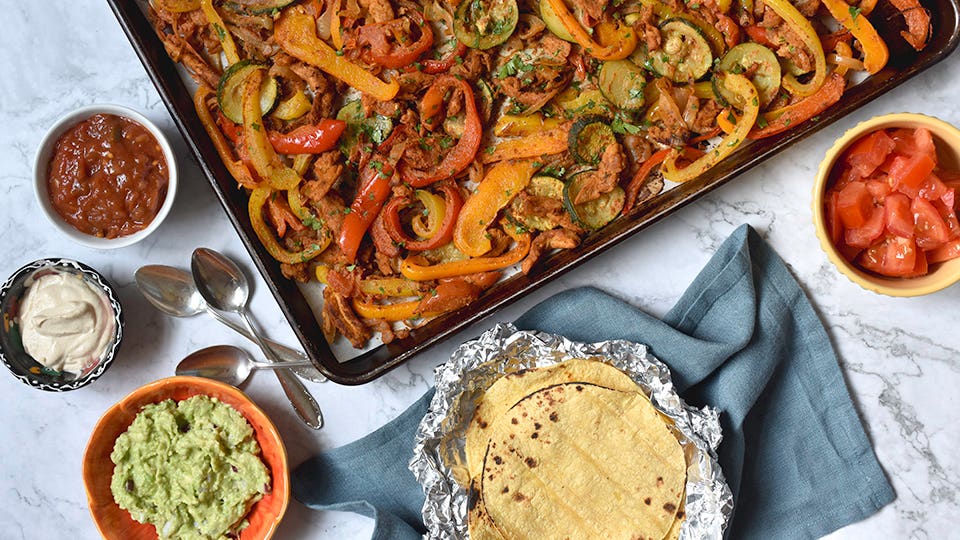 A sheet pan supper featuring soy curls, with tortillas, salsa, guacamole and vegan sour cream and tomatoes laid out beside it