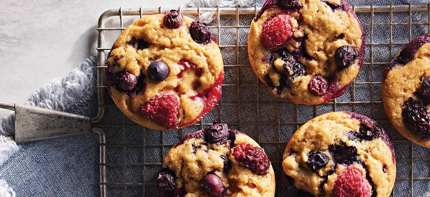 Five fresh-baked Triple Berry Muffins on a wire cooling rack