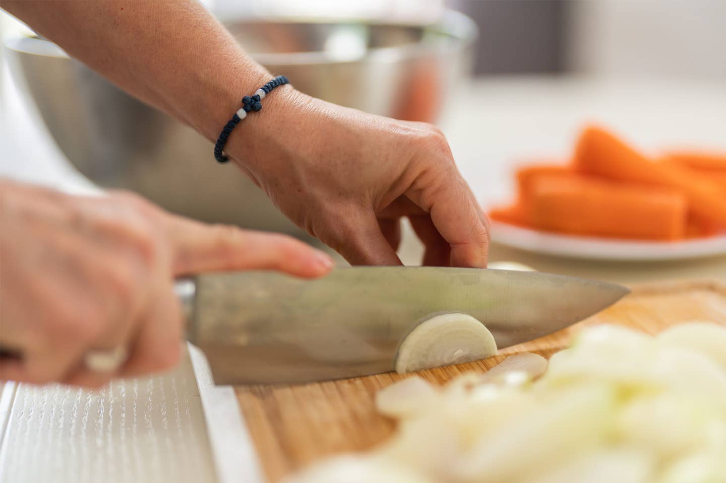 unidentified hands making mirepoix, cutting onion on a chopping board with a plate of carrots in the background