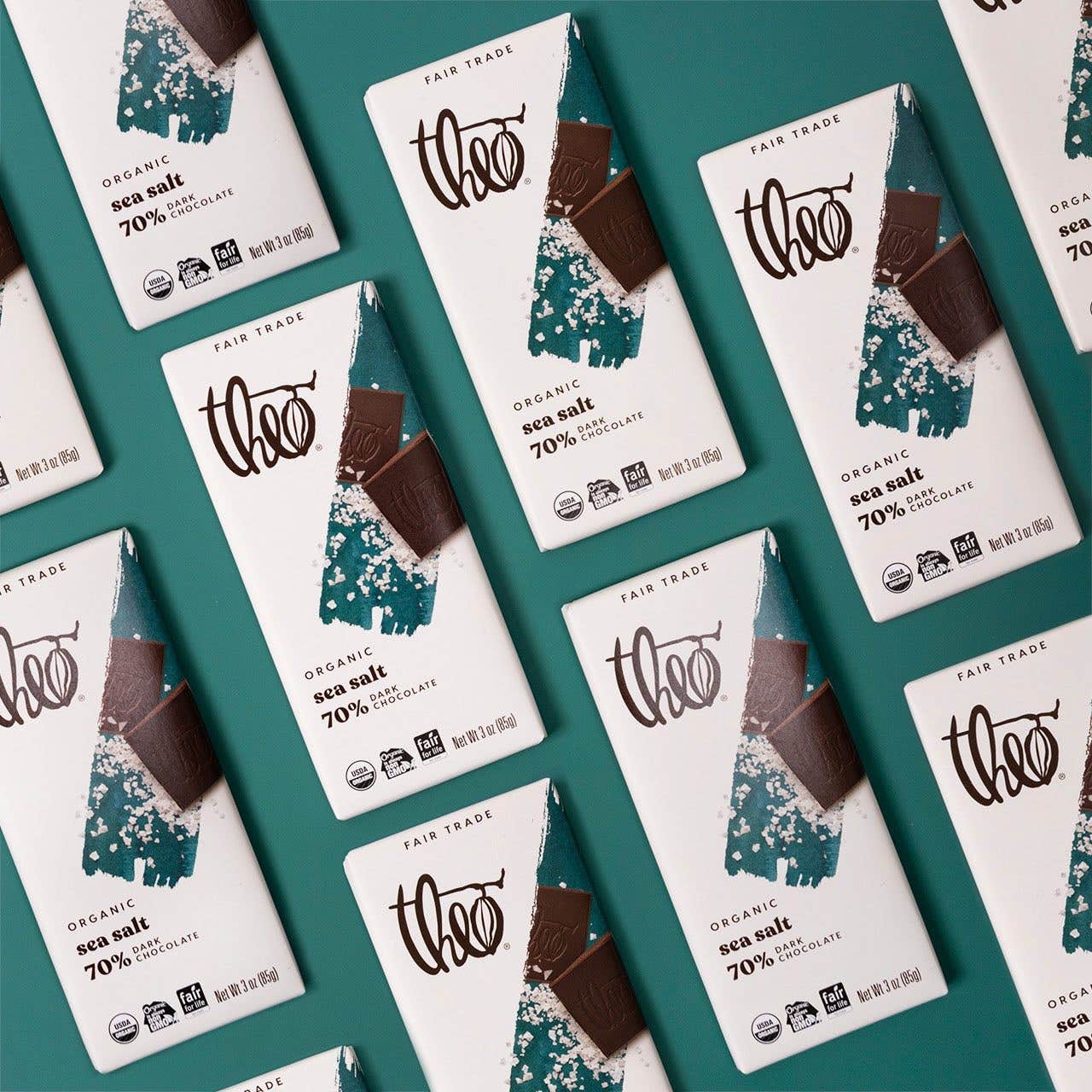 Many Theo sea salt vegan dark chocolate bars, laying in parallel lines on a solid green background