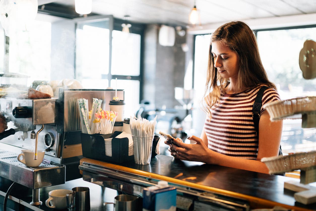 Young woman looks at her phone while waiting for her order at a chain coffee shop