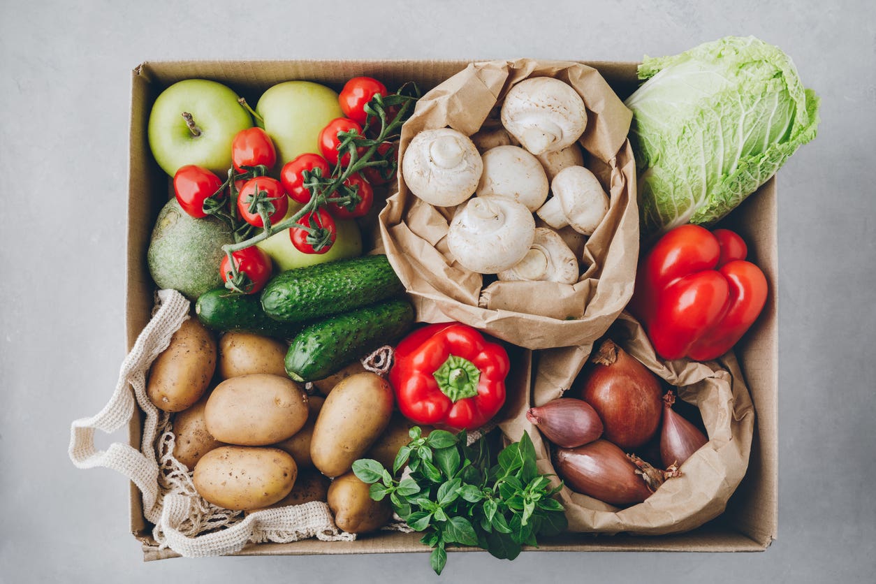 Box of farm-fresh produce including tomatoes, potatoes, cucumbers, radish, basil, onions, paprika, lettuce. 