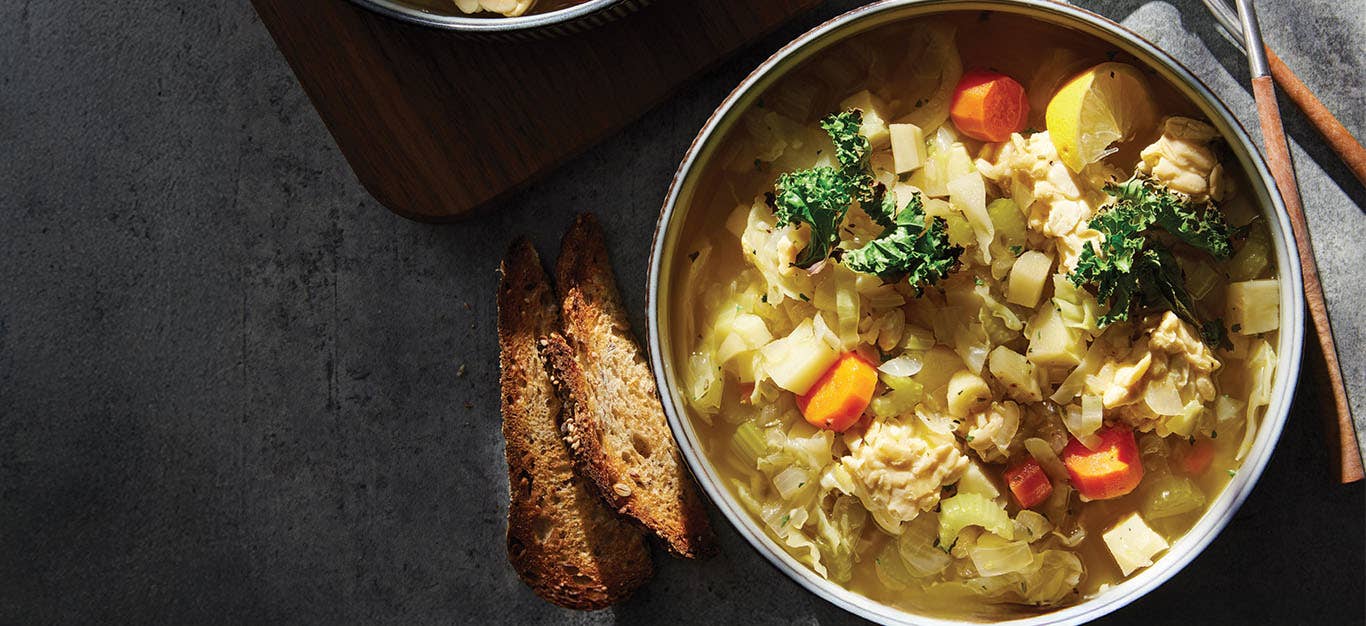 Cabbage Stew with Tempeh and Crispy Kale in a ceramic serving bowl with crusty bread on the side