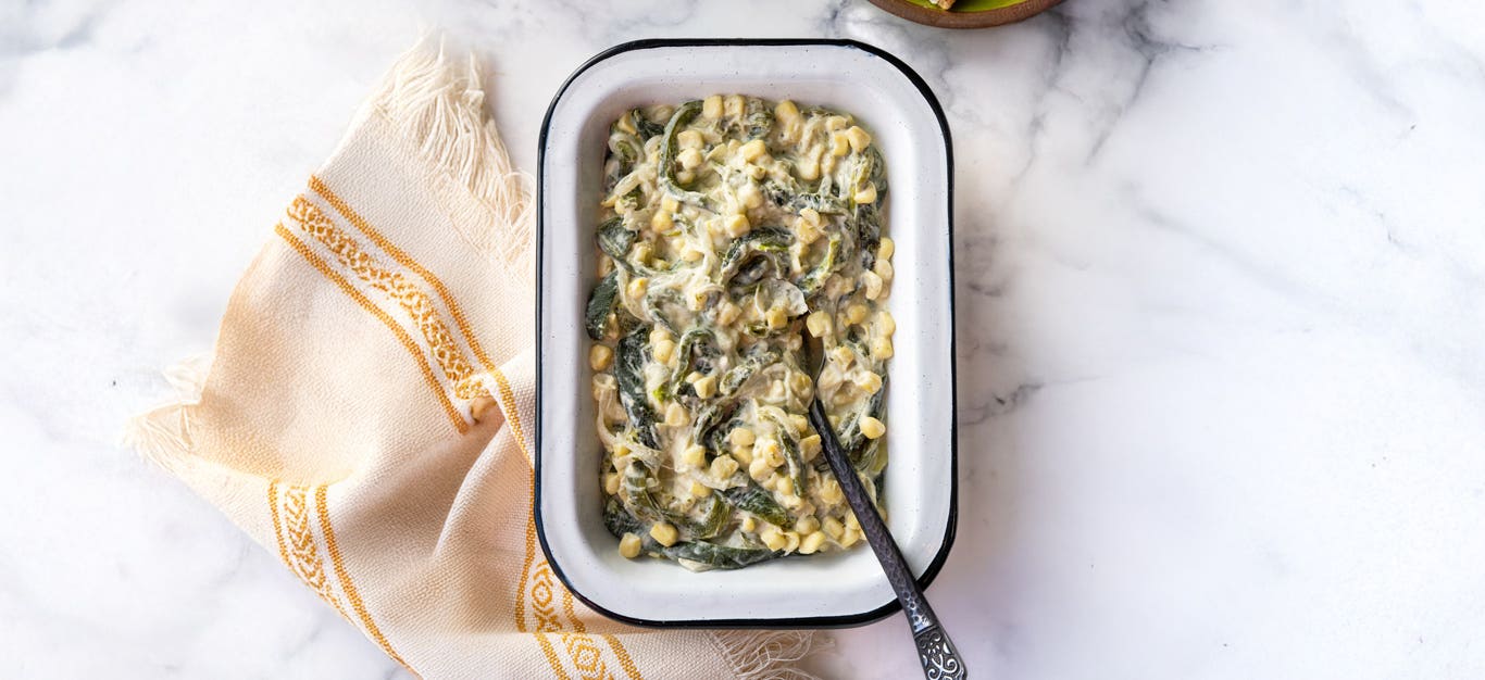 A white baking dish full of creamy poblano and corn filling, with a spoon in the dish