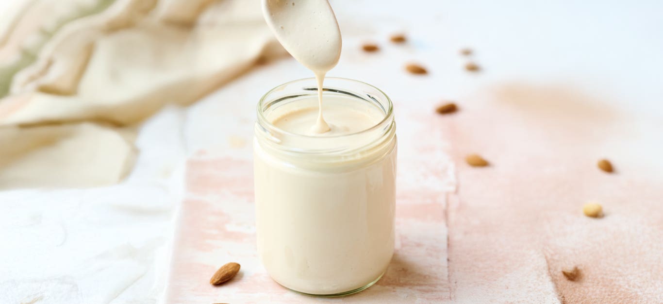 Almond Crema (Crema de Almendras) in a glass with a white jug above, pouring in crema