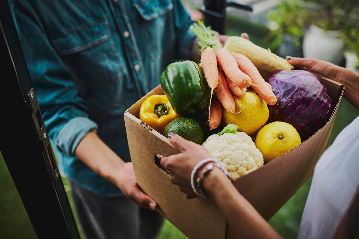 A woman hands another woman a CSA (community-supported agriculture) box full of fresh produce