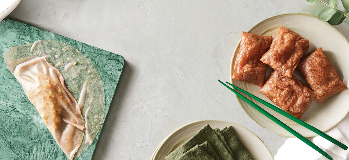 A plate of cooked Air-Fryer Rice Paper Dumplings on the right, and on the left you can see a dumpling partially wrapped on a green plate