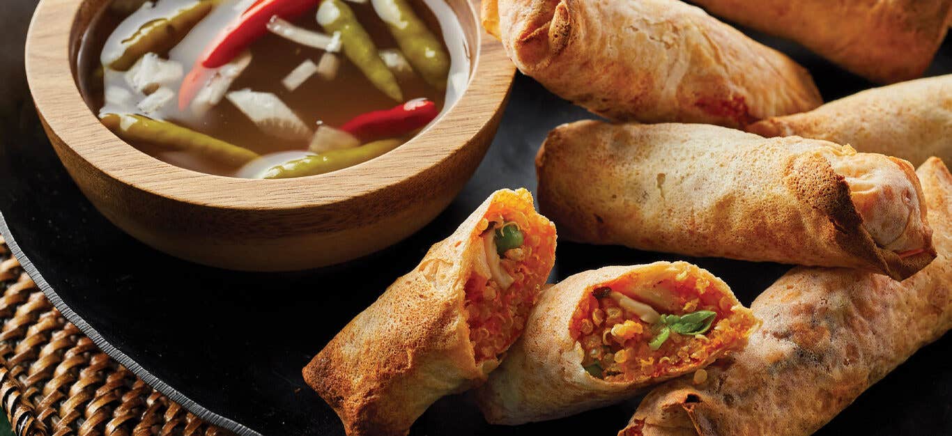 Air-Fried Vegan Lumpia on a black plate with a bowl of dipping sauce