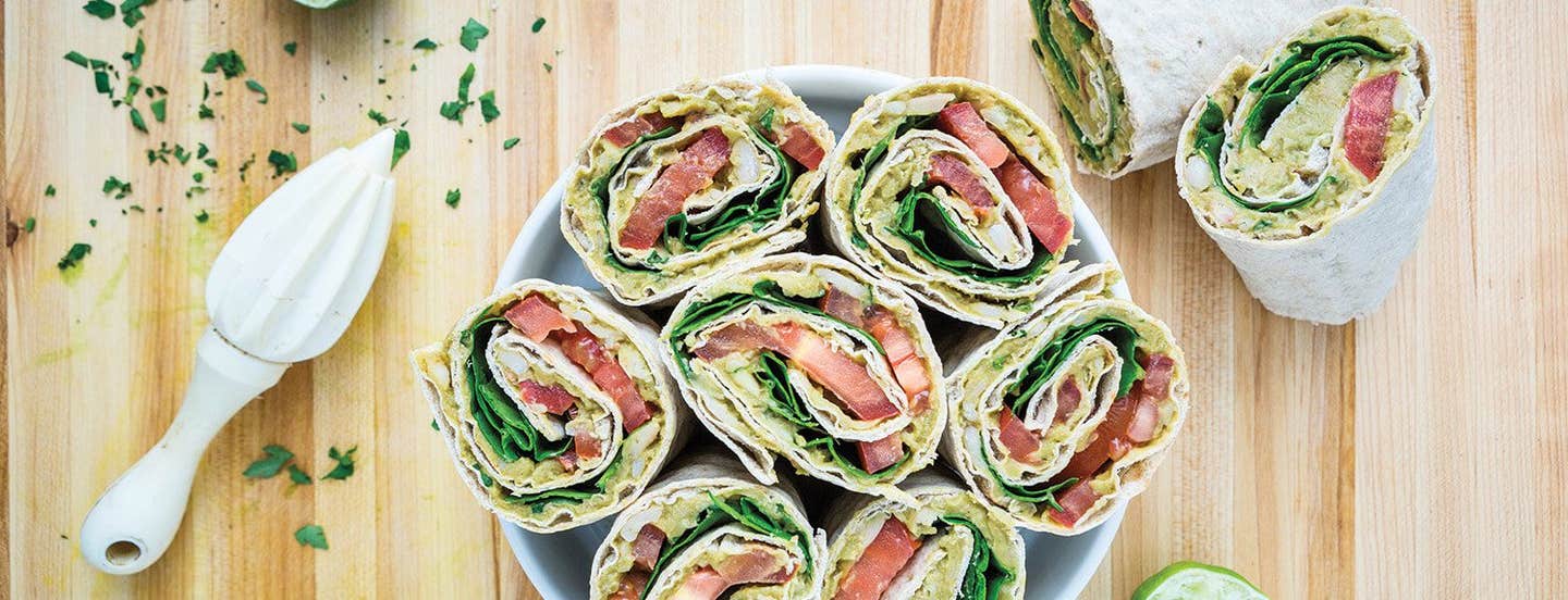 Four Avocado & White Bean Salad Wraps cut in half with the cut side face up, in a white bowl with a a hand-held lemon squeezer to the side