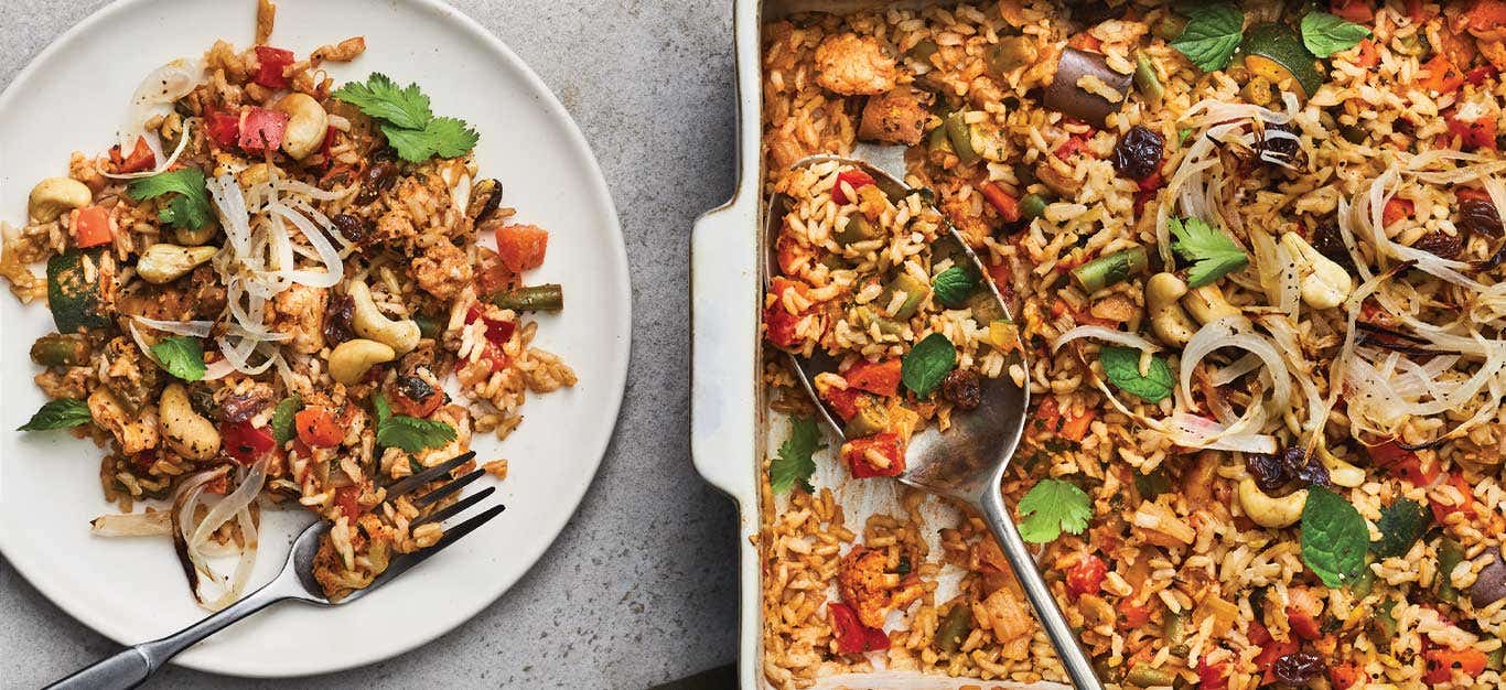 Baked Vegetable Biryani in a casserole dish next to a white plate with a full serving and metal fork