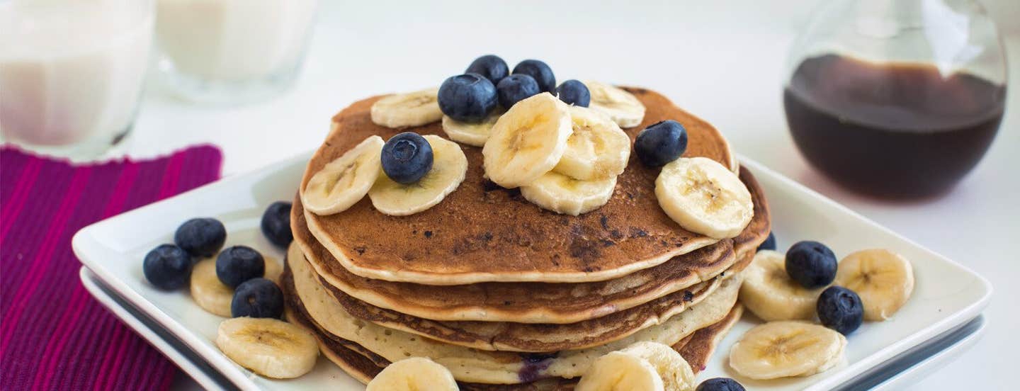 A stack of Banana Pancakes on a plate with fresh blueberries and banana slices