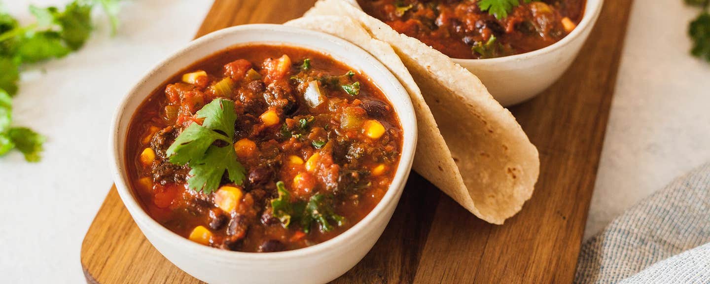 Two bowls of Black Bean and Corn Chili on a wooden chopping board with a warm tortilla folded