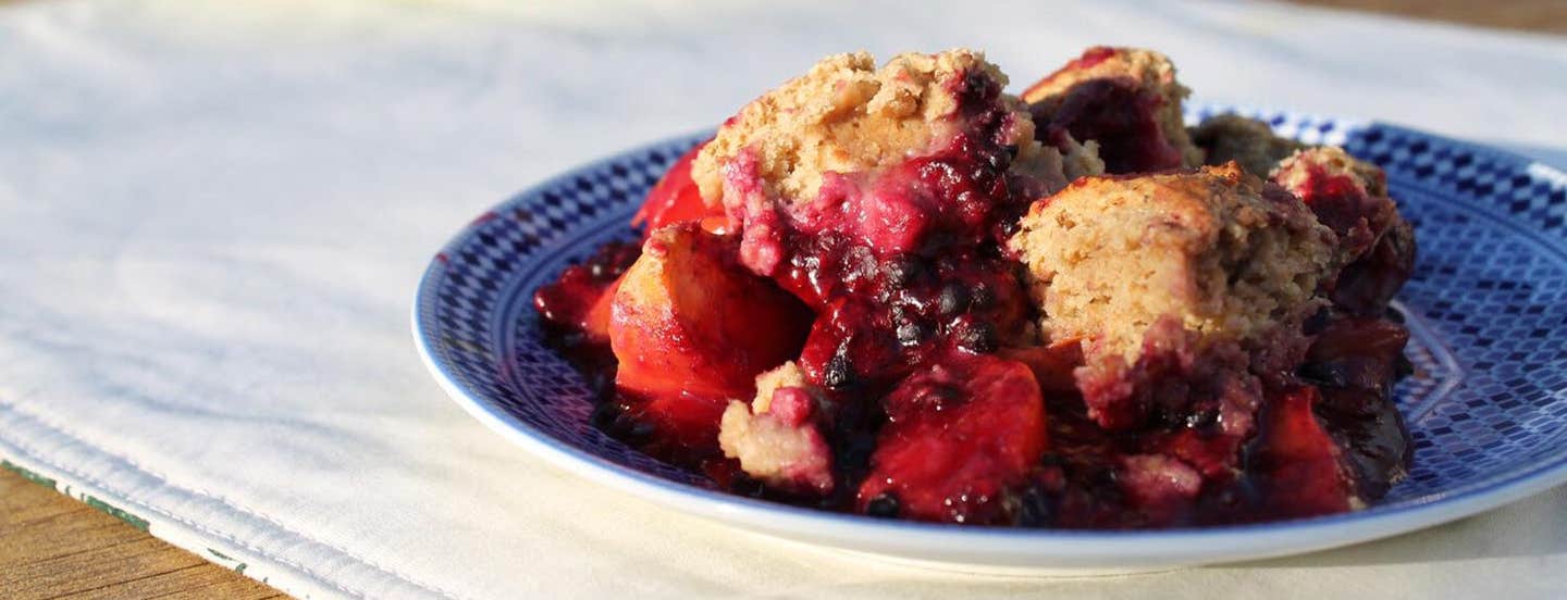 A serving of Blackberry Peach Cobbler on a blue plate on a white cloth