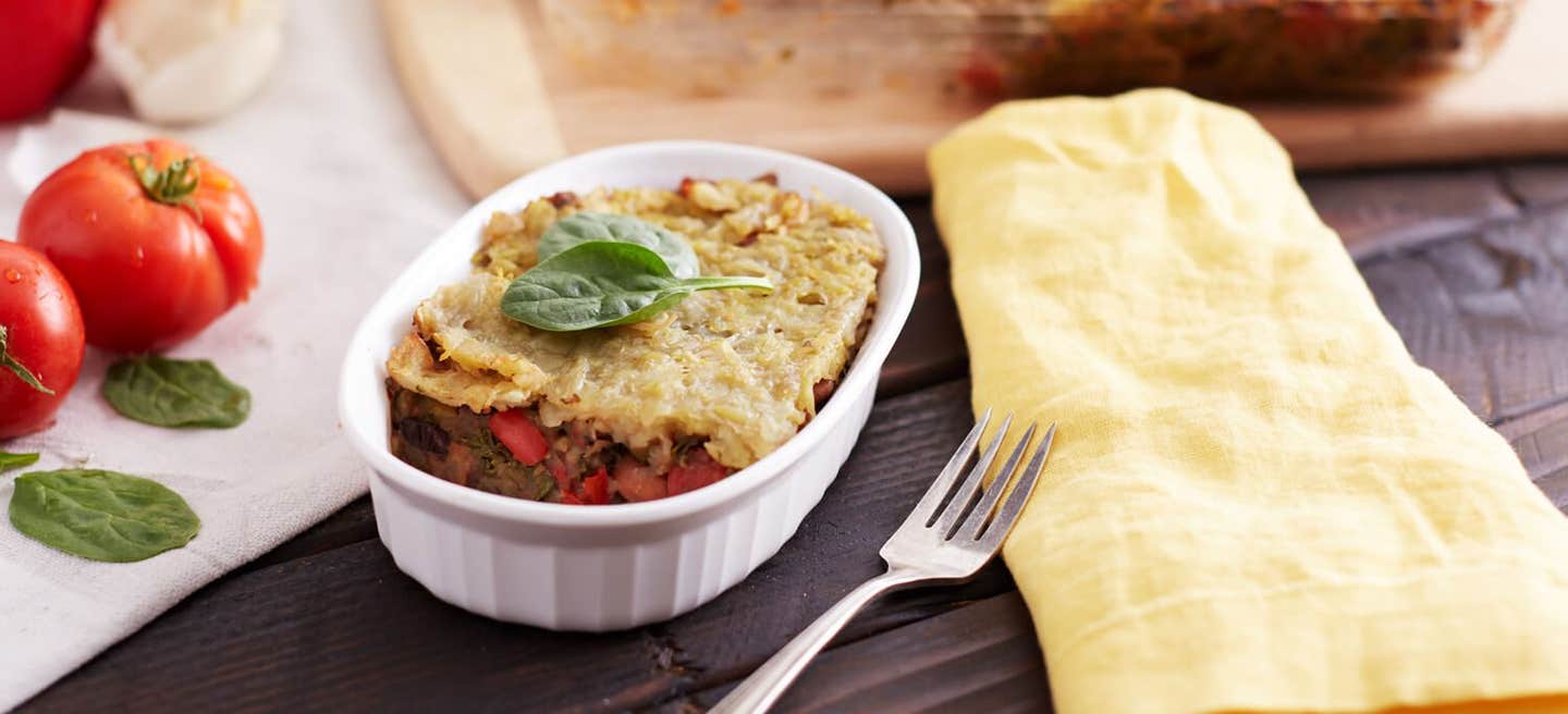 Breakfast Burrito Bake in a single serve, white, oval dish, garnished with a sprig of basil, next to a yellow cloth napkin and a fork