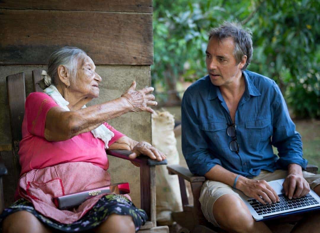 Dan Buettner sitting with a lap top on his lap talking to a very old woman