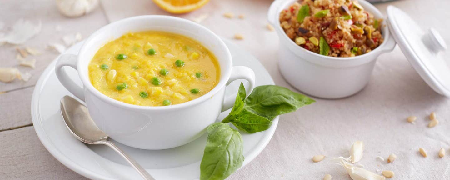 Butternut Squash Soup with Peas in a white bowl on a white plate with a sprig of basil on the side