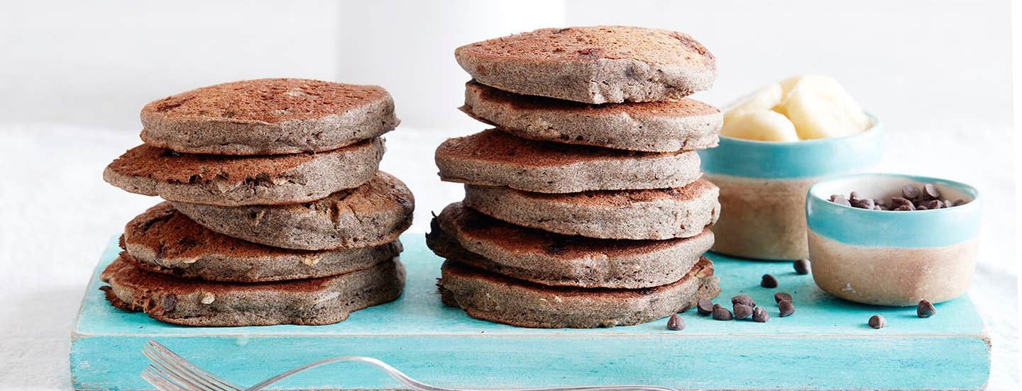 Two large stacks of Chocolate Chip Coconut Pancakes next to a bowl of sliced banana and a small bowl of vegan chocolate chips