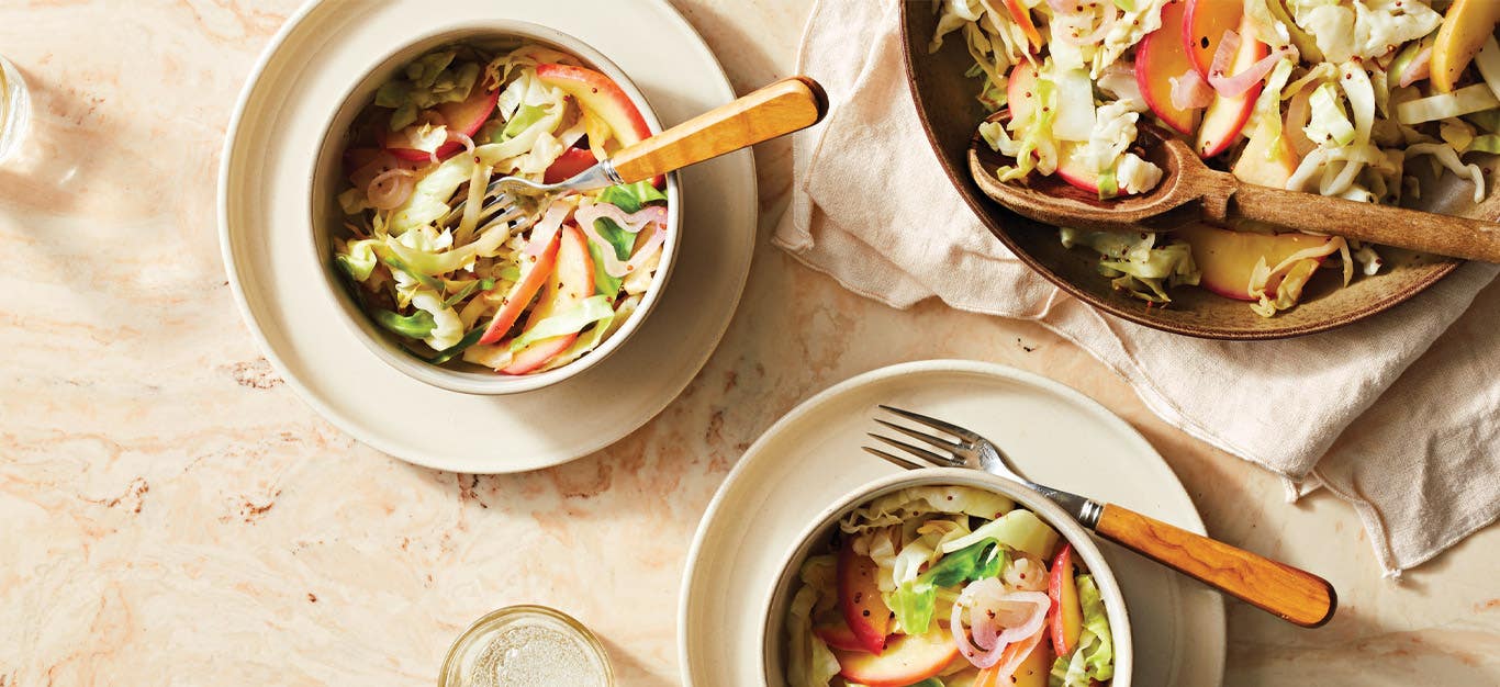 Tangy Cabbage and Apple Sauté in small white bowls with forks against a beige marble countertop