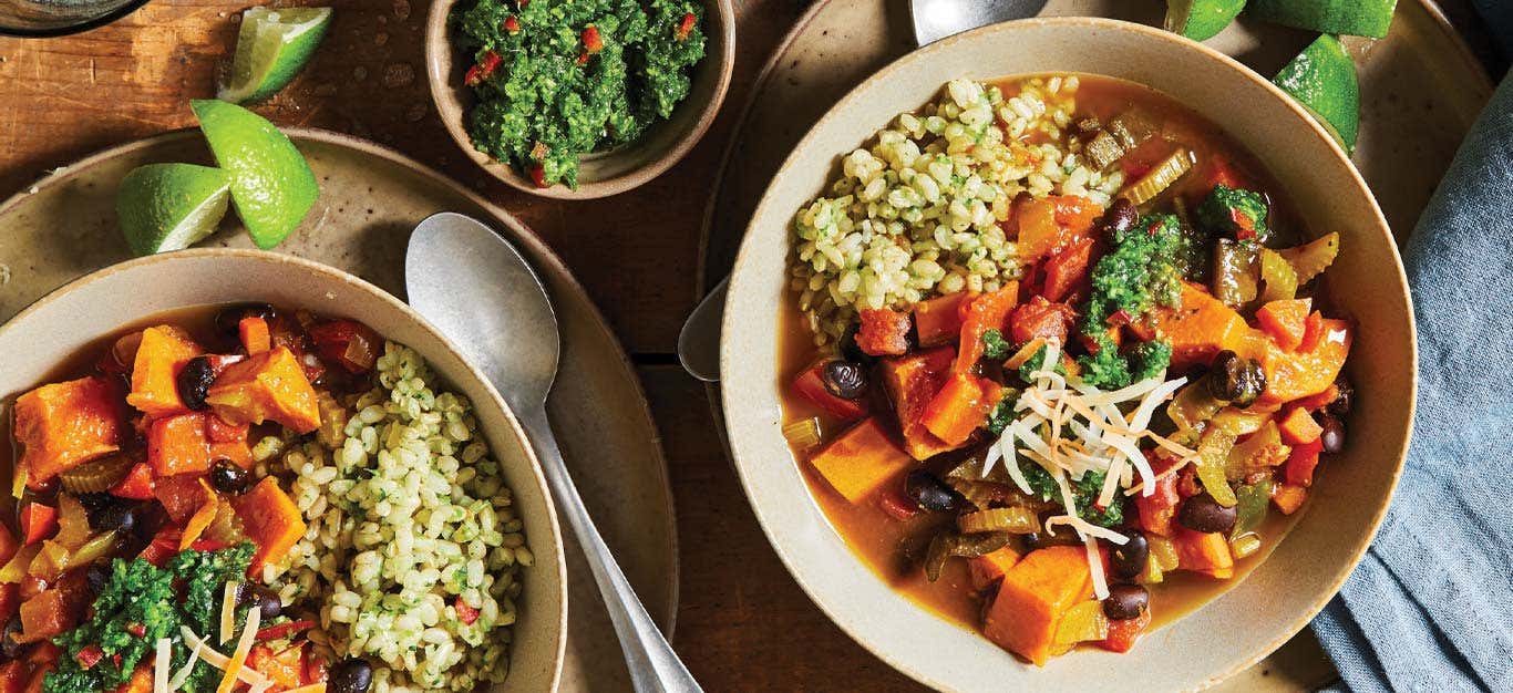 Caribbean Sweet Potato Stew in tan ceramic bowls with a side of green sauce in a small bowl