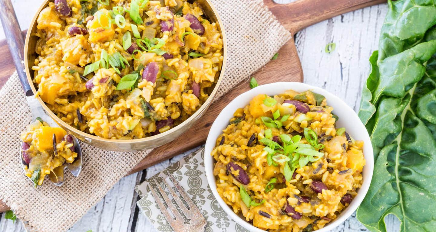 A large bowl of Caribbean Rice on a wooden chopping board with a smaller bowl on the counter