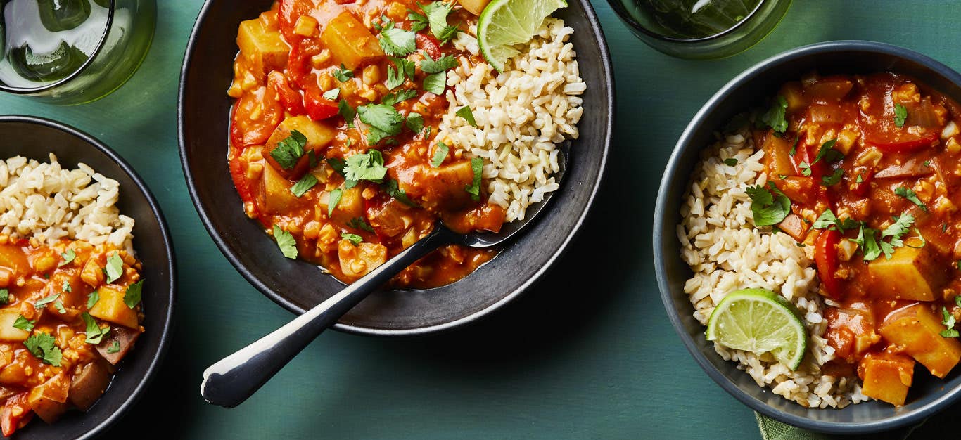 Vegan Red Curry with Cauliflower and Potatoes in gray ceramic bowls with metal spoons against a blue countertop