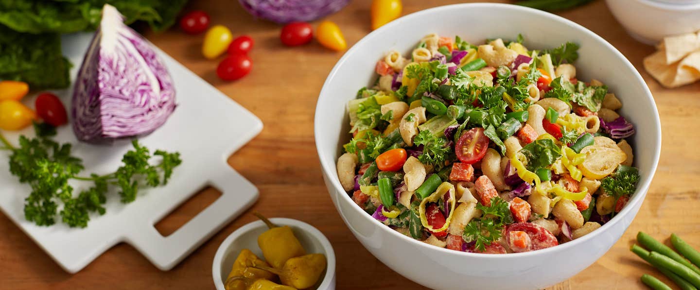 Chopped Veggie Salad with Pasta and Creamy Cauliflower Dressing in a white bowl with fresh veggies in the background