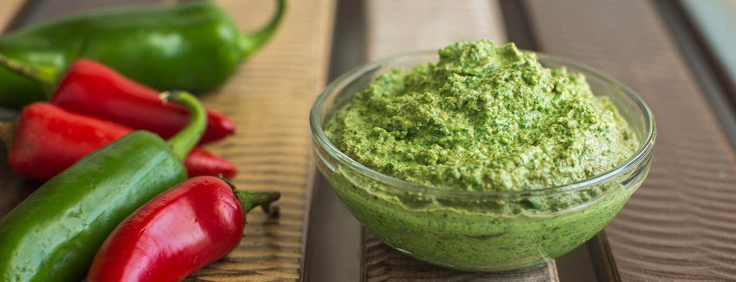 A small glass bowl of Spicy Cilantro Pesto next to fresh green and red chiles