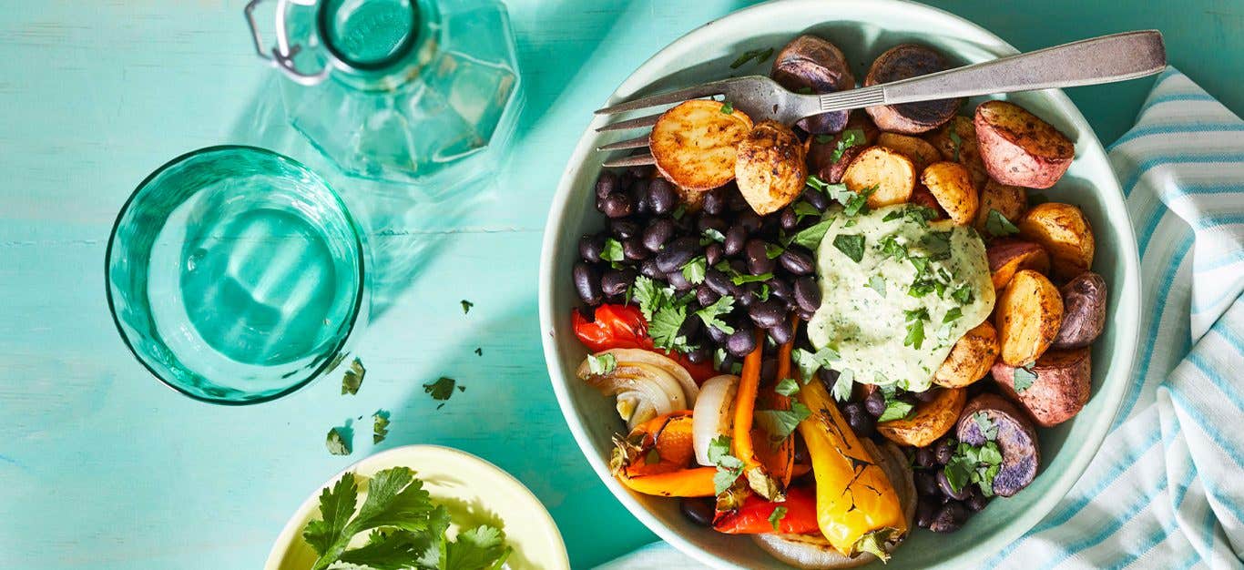 Cilantro-Sauced Roasted Potato Bowl with a sprinkle of fresh cilantro on a blue table with glasses of water