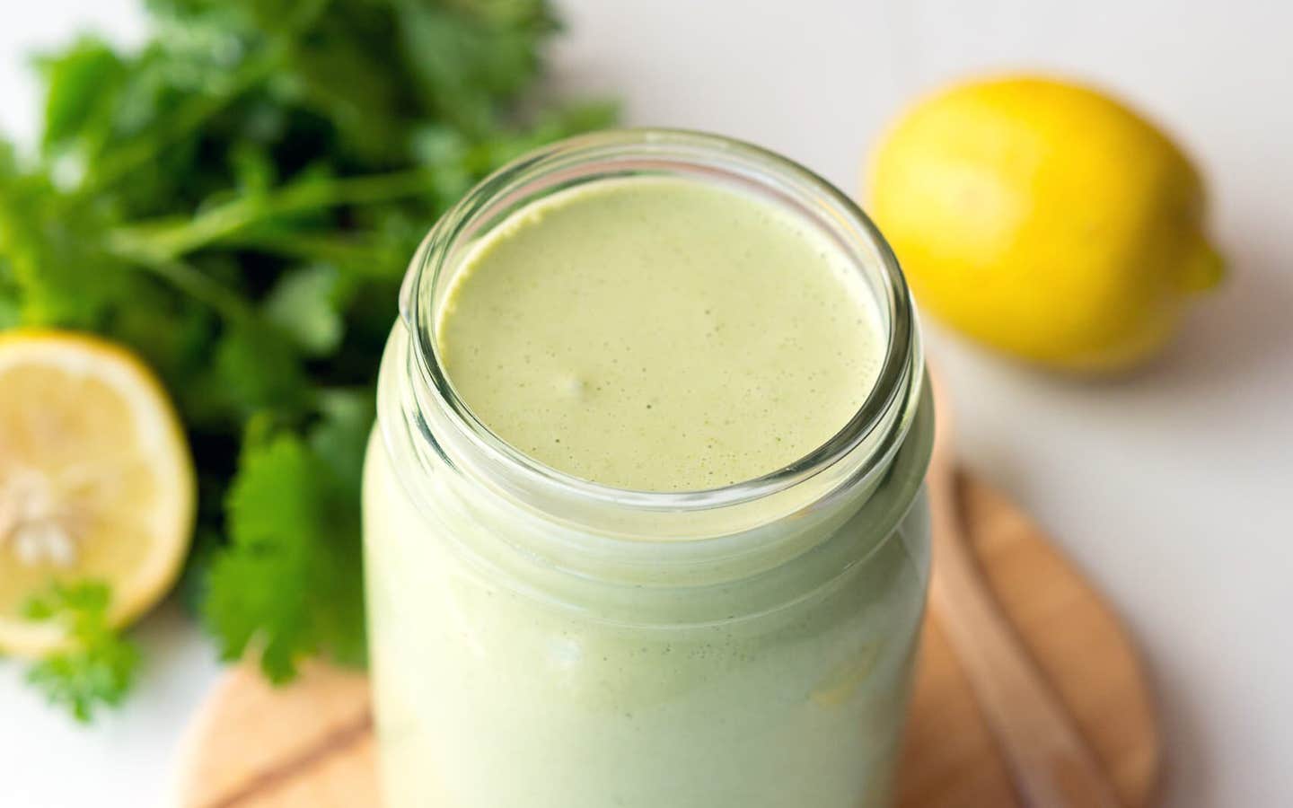 Cilantro-Cashew Dressing in a mason jar with fresh cilantro and lemon in the background