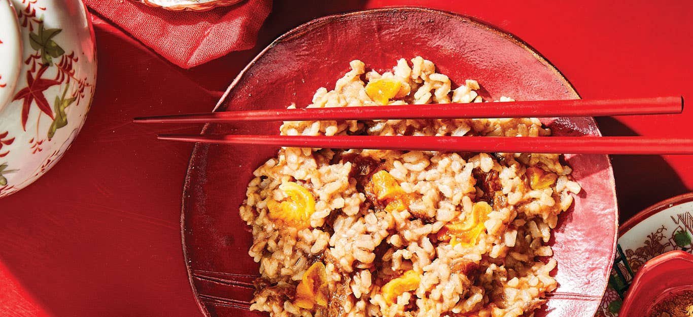 Sweet Congee with Dates and Apricots in a red bowl with red chopsticks against a red background