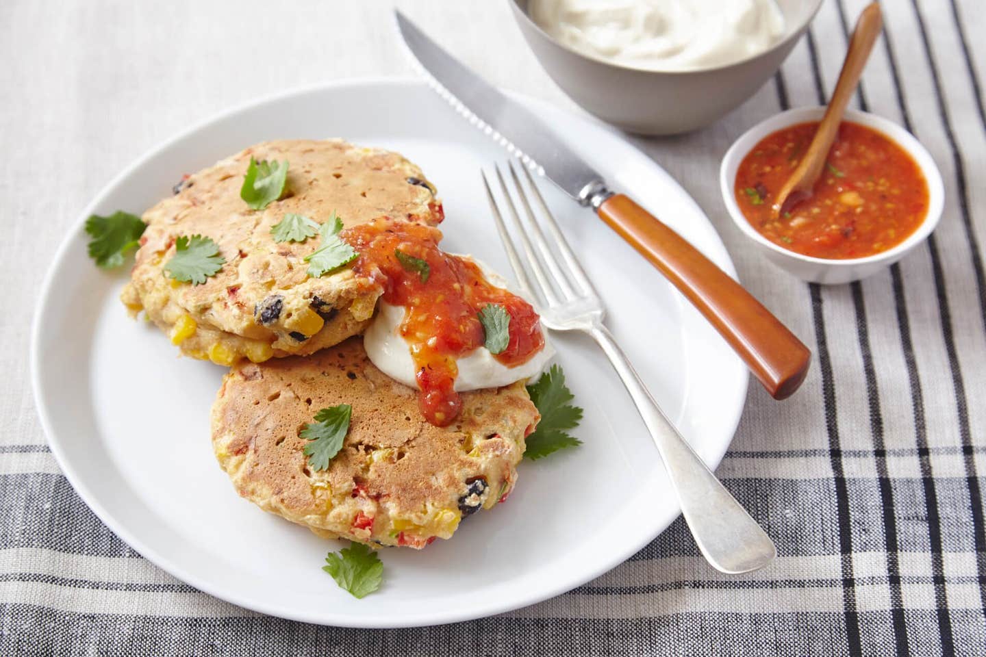 Two Corn and Black Bean Cakes with a dollop of vegan sour cream and a drizzle of salsa on a white plate