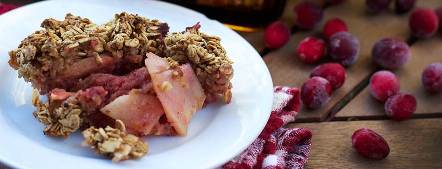 Cranberry Apple Crisp on a plate with a red and white checked cloth napkin and fresh cranberries to the side