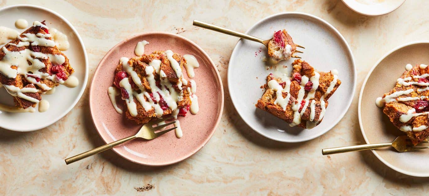 Cranberry-Orange Bread Pudding on white and pink plates drizzled with a creamy sauce