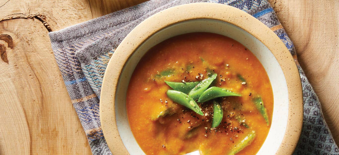 Creamy Carrot and Pea Soup in a white and tan bowl on a blue cloth napkin