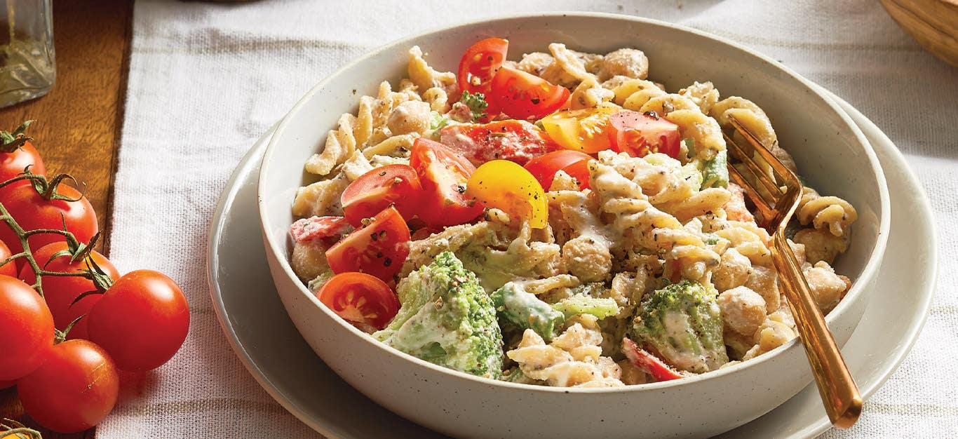 Healthy Creamy Pasta with Veggies and Chickpeas in a white ceramic bowl with gold metal fork