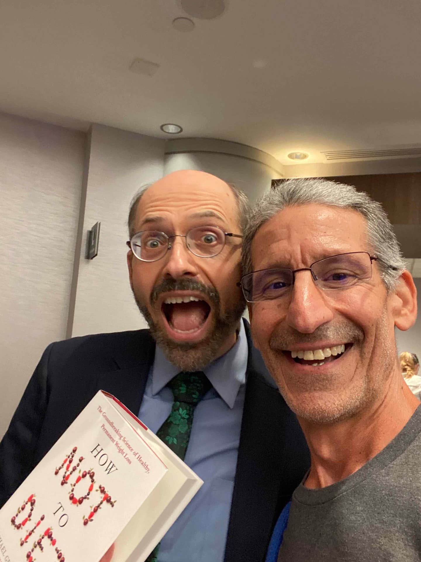 Dr. Michael Greger poses with plant-based fan Rich Ferrandino while holding a copy of his book How Not to Diet