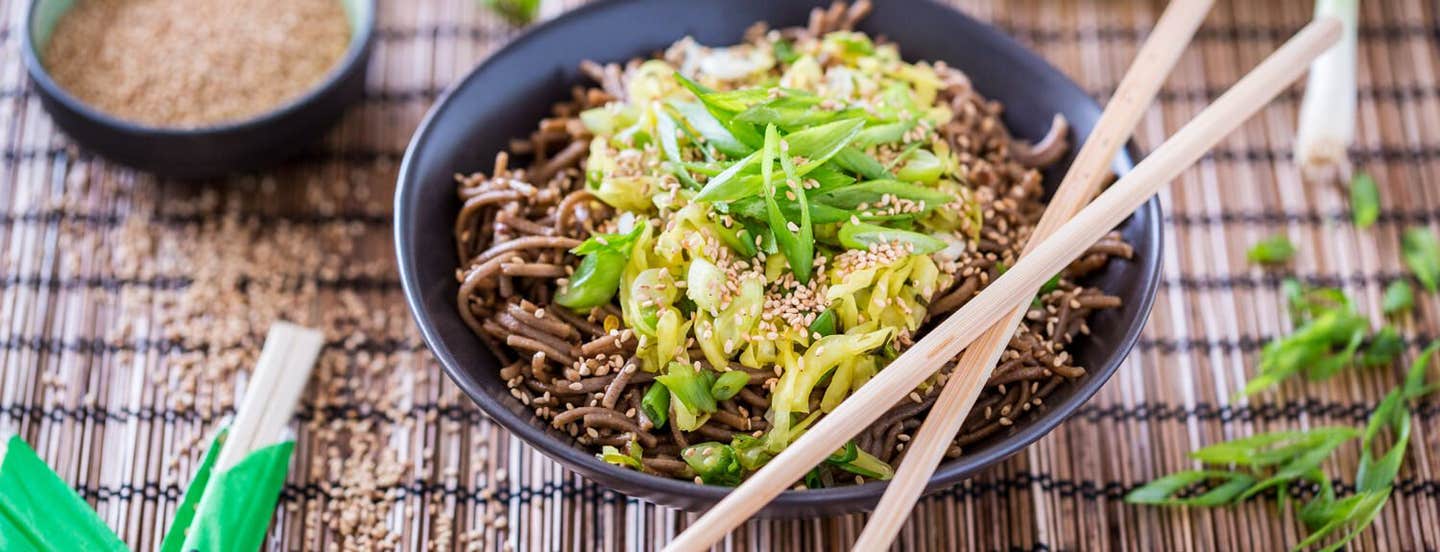 Dan Dan Mian Noodles in a black serving bowl on a grass mat with chopsticks on the bowl