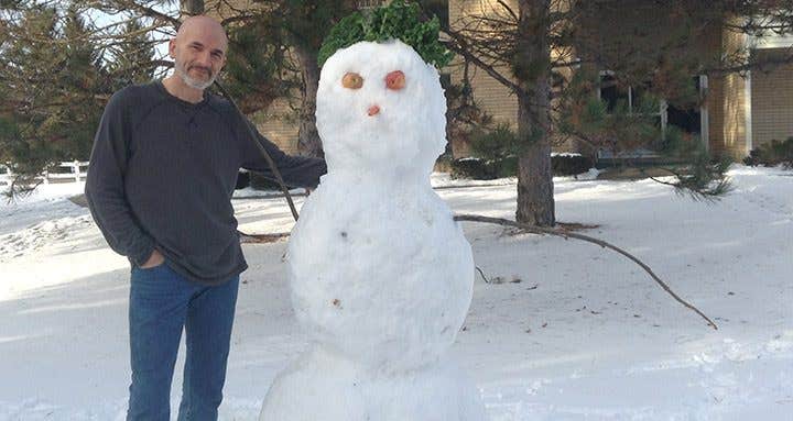 Dave Willits standing outside with is arm around a snowman. the snowman has apples for eyes, a carrot for a nose and kale for hair.